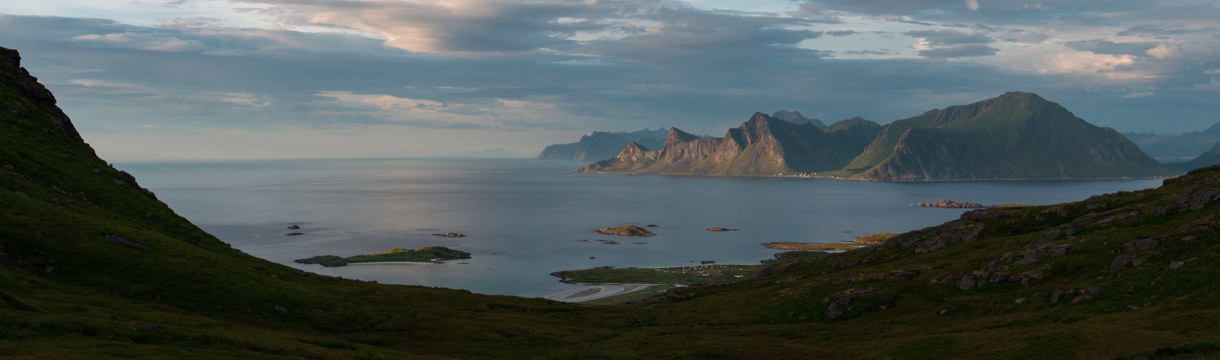 Panoramic view across a calm fjord towards distant mountains in the Lofoten Islands